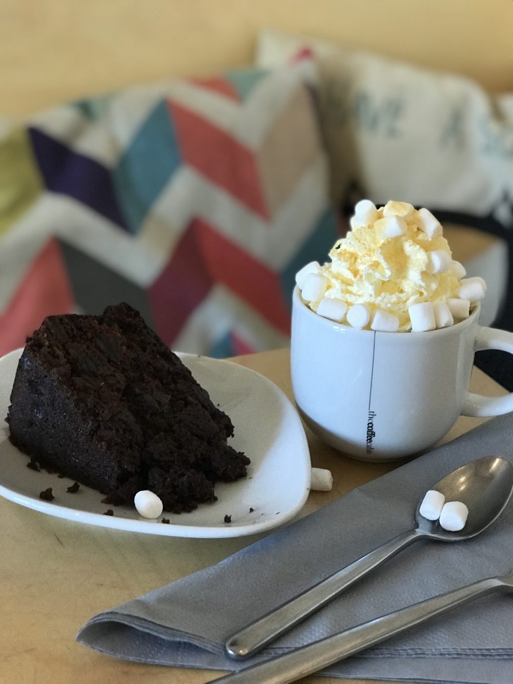 Chocolate cake with cream beside a hot chocolate with marshmallows