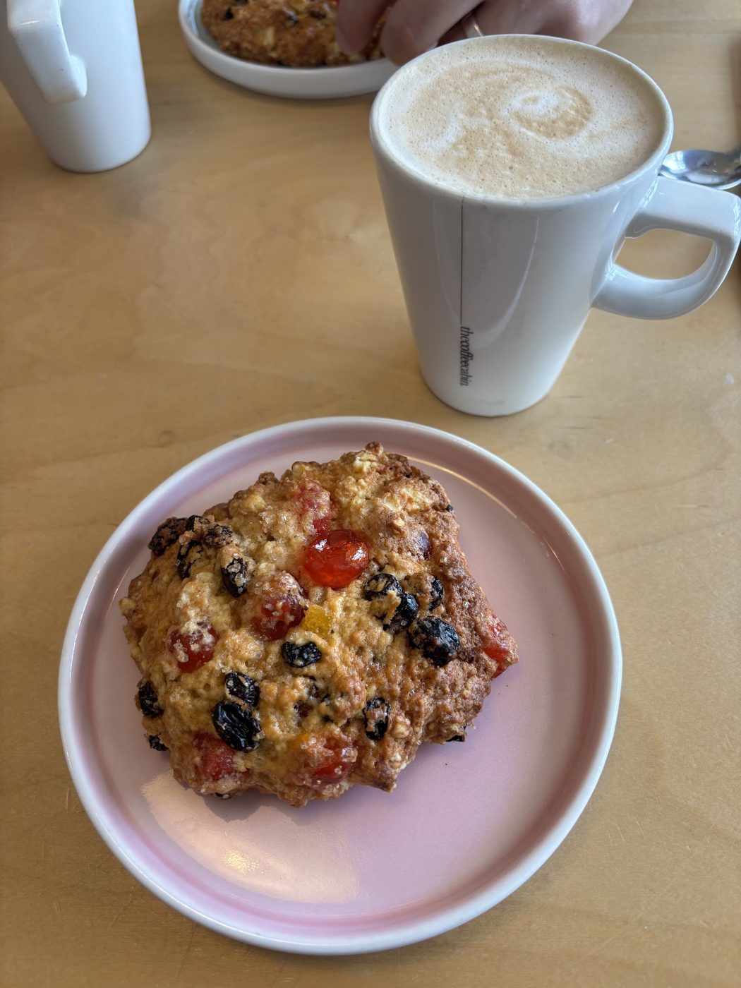 A fruit scone with a latte behind