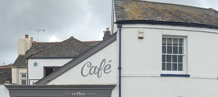The white building with the grey “Café” lettering above the thecoffeecabin sign